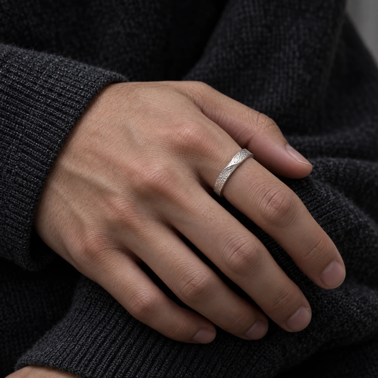 Silver Mobius ring worn on an index finger with a charcoal knit sweater